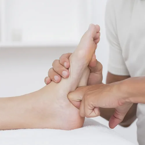 Manos realizando una sesión de reflexología podal en los pies, aplicando presión en puntos energéticos para promover el equilibrio y la relajación